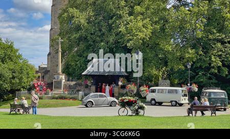 A vintage white Volkswagen Beetle adds charm to a wedding scene in Sedgefield, UK, set against a historic church and formal gathering Stock Photo
