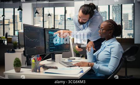 Teamworking proprietary firm colleagues using deep learning to assess stock market volatility. Brokerage company supervisor and african american woman using AI to generate investment reports Stock Photo