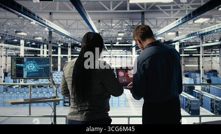 Team of server room technicians alerted by warning message on laptop causing infrastructure slowdowns. Teamworking data center colleagues see malfunction popup caused by software errors, camera A Stock Photo