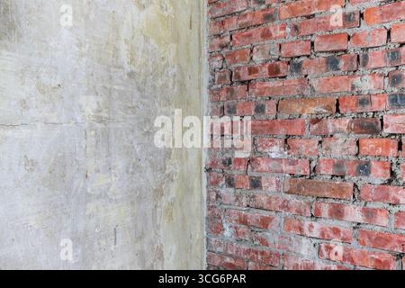 Old textured wall with cracked plaster meeting a rough red brick surface. Rustic industrial background showing raw materials, contrast of concrete and Stock Photo