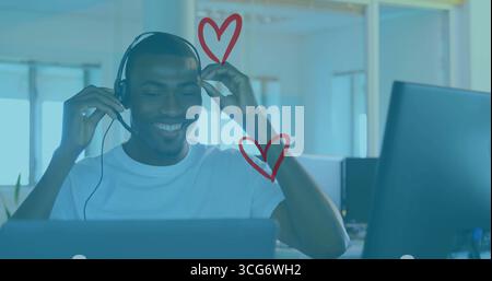 Smiling worker wearing white Tshirt using laptop and headset in office, with heart graphics Stock Photo