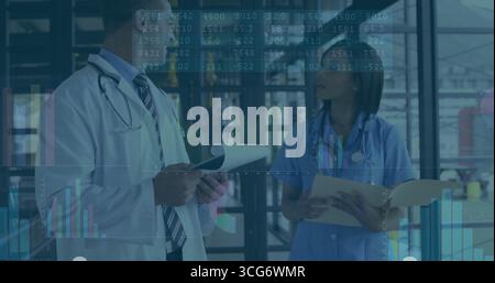 Reviewing papers two staff wearing lab coat and scrubs discussing data in hallway, with stethoscope Stock Photo