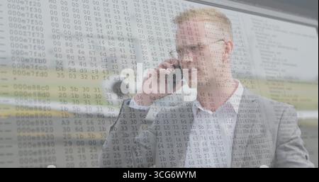 Man in gray suit speaking into smartphone in office, with desk microphone, code overlay, copy space Stock Photo