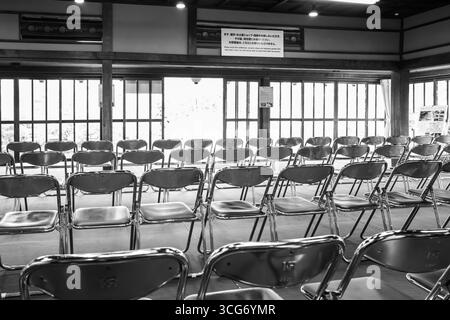 A black-and-white photograph capturing a quiet interior with rows of folded chairs and traditional wooden architecture, highlighting a tranquil, empty Stock Photo