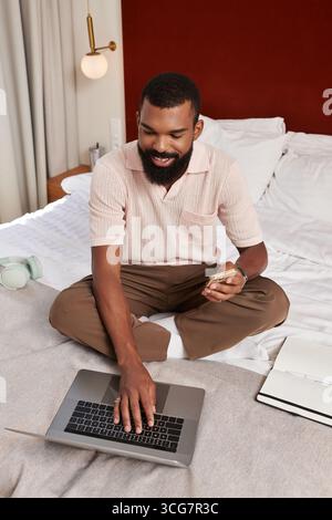 A charming man is sitting comfortably in his hotel room, working on his laptop. Stock Photo