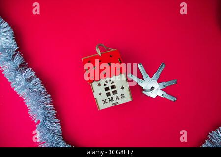 On a red background lies a Christmas house and a bunch of keys. Space for text. Stock Photo