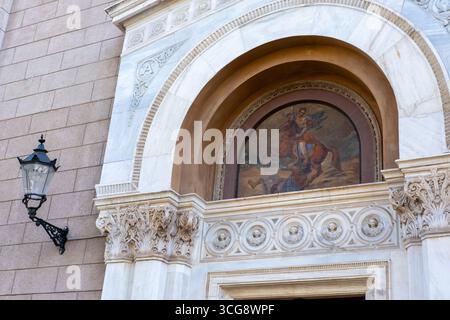 View of an ornate marble archway frames a vibrant painting of a horseman, contrasting with the textured stone wall and a vintage street lamp, Athens, Stock Photo