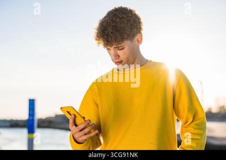 Young man using smartphone by the sea at sunset Stock Photo