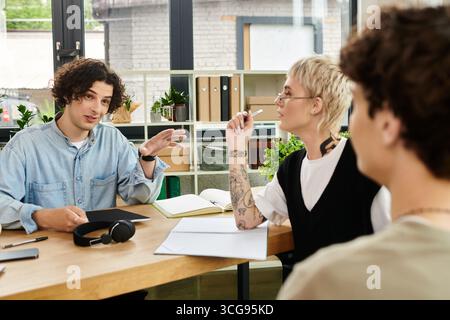 Three young individuals collaborate enthusiastically, sharing ideas in a modern workspace. Stock Photo