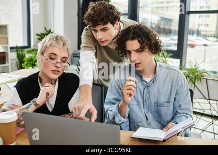 Three young professionals collaborate at a modern office desk, discussing and solving problems. Stock Photo