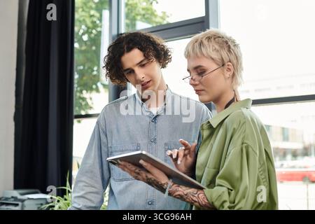 Two young professionals collaborate on a project while discussing ideas and reviewing materials. Stock Photo