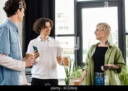 Three young professionals share coffee and ideas in a lively office while collaborating. Stock Photo