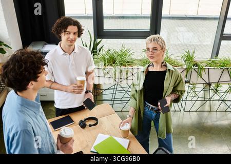 Three young workers share ideas over beverages in a vibrant office environment. Stock Photo