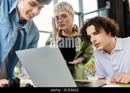 Three young individuals engaged in a dynamic discussion while examining a laptop screen together. Stock Photo