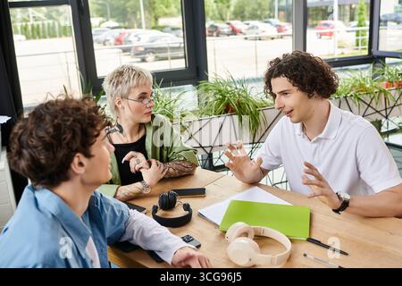 Three young professionals engage in a dynamic discussion at a bright office table, sharing ideas. Stock Photo