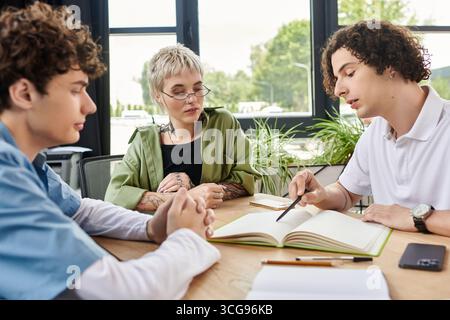 Three young professionals engaged in a discussion while working on a project at a table. Stock Photo