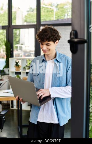 A man is focused on typing on a laptop while standing in a contemporary office setting. Stock Photo