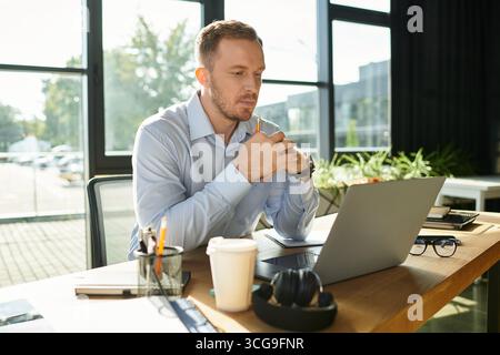 A young professional is deeply engaged with his laptop and thoughtfully contemplating his tasks. Stock Photo