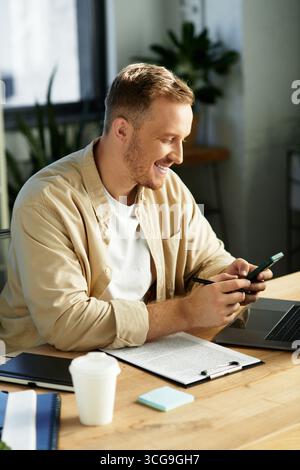 A young businessman smiles while using his phone, immersed in his work at a stylish office. Stock Photo