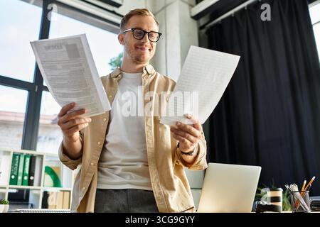 A stylish young man in an office reviews documents while contemplating work decisions. Stock Photo
