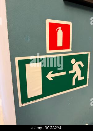 Fire extinguisher and emergency exit signs on a blue wall for safety guidance background. Mobile photo Stock Photo