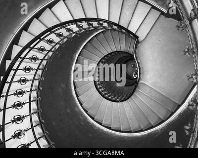 Elegant spiral staircase in a monochromatic tone viewed from above, showcasing intricate railing design and graceful architectural curves. Stock Photo