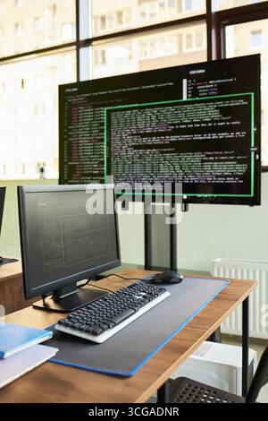 Modern workspace featuring desktop computer and large monitor displaying programming code, suggesting software development or coding environment in contemporary office setting Stock Photo
