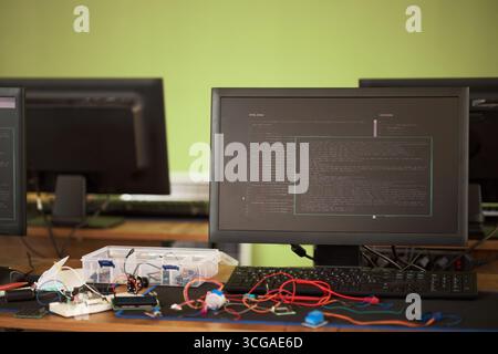 Closeup showing desktop computer monitor displaying programming code with electronic components and circuit boards on desk, suggesting technology development or engineering workspace Stock Photo
