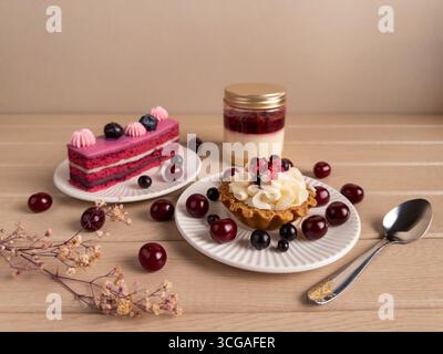 A beautifully arranged assortment of desserts including a layered cake, a tart, and a jar dessert, garnished with fresh berries on white plates Stock Photo