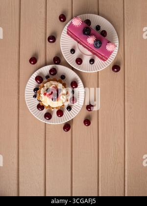 A top-down view of elegantly plated desserts with fresh cherries and blueberries on a rustic wooden background, perfect for food related content Stock Photo