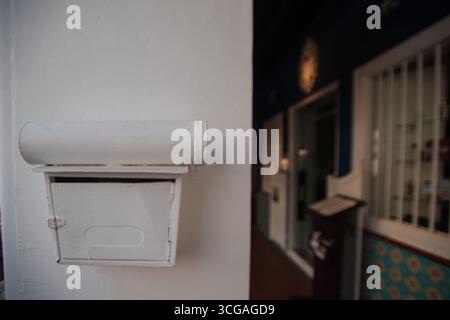A white mailbox is mounted on a wall, with visible mail inside and slightly worn paint on the top lid. Stock Photo