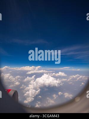 View from airplane window scattered white clouds floating above a vast landscape, with winding rivers below. The deep blue sky and soft cloud formatio Stock Photo