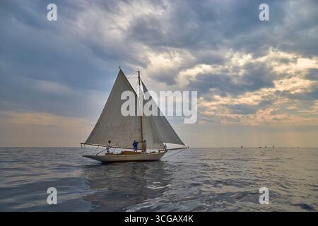 Sailing Boat Drifting Along on an Open Sea Under a Vibrant Evening Sky Stock Photo