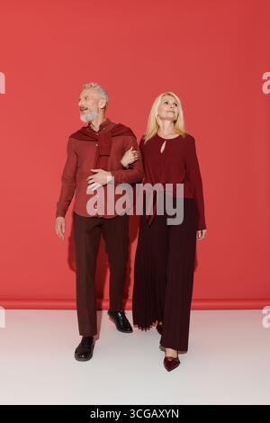 A couple walks hand in hand, showcasing their elegant outfits and joyful connection. Stock Photo