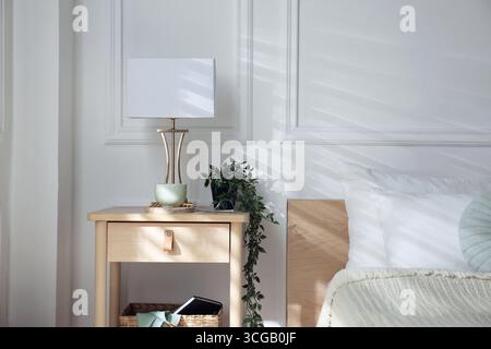 Bedside table with lamp and other decor near bed indoors Stock Photo