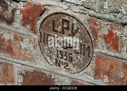 Liepaja, Latvia - May 04, 2013 - Rusty circular metal plate on weathered brick wall with moss and lichen. Stock Photo