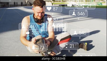 Adjusting prosthetic leg, man sitting on blue track wearing sportswear, floating social media icons Stock Photo