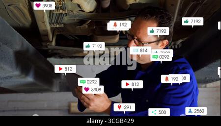 Inspecting car underside on lift, mechanic in coveralls using tablet in shop with icons, copy space Stock Photo
