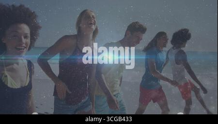 Strolling five friends laughing, smiling at sandy shore edge, with lens flare and starry overlay Stock Photo