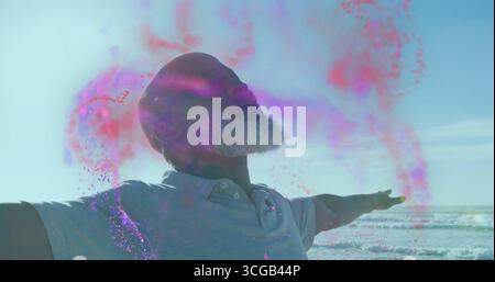 Man wearing polo shirt spreading arms tilting head at beach, with pink and purple powder swirl Stock Photo