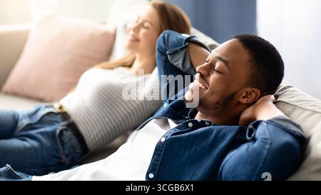 Happy Interracial Couple Leaning Back On Couch While Relaxing At Home Together Stock Photo