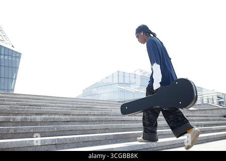 Young Adult Black Man Walking Upstairs Carrying Guitar Case Outdoors Stock Photo