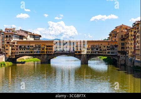 Historic Ponte Vecchio bridge in Florence, Italy, spans the Arno River with charming shop-lined architecture under a clear blue sky. Stock Photo