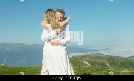 Dance on a grassy mountain peak under clear blue sky, celebrating love and freedom in nature. Stock Photo