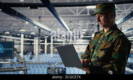 Army software developer in server hub uses artificial intelligence app on laptop to review reconnaissance information. Military data center employee uses neural networks to plan mission, camera A Stock Photo