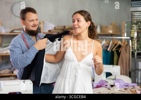 Female client trying on custom blazer with tailor in workshop Stock Photo