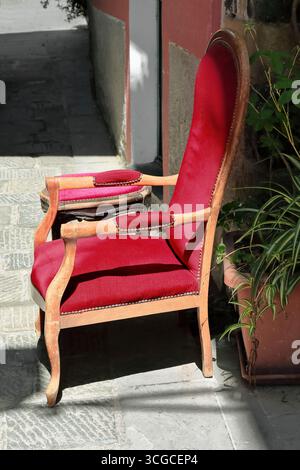 258 Red velvet upholstery, wood armchair and footstool next to a house on Via Vittorio Emanuele Street east side, old town. Monterosso al Mare-Liguria Stock Photo