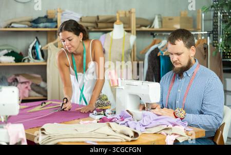 Tailor sewing with colleague cutting fabric in modern studio Stock Photo