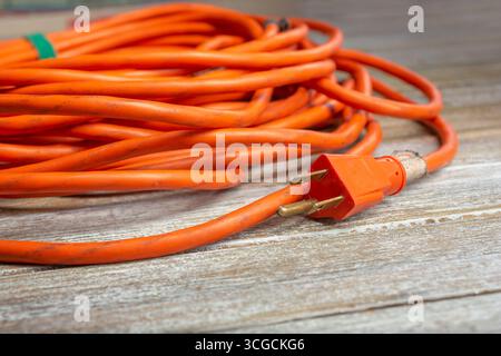 A closeup view of a wrapped orange extension cord featuring the male prong plug, on a wooden surface. Stock Photo