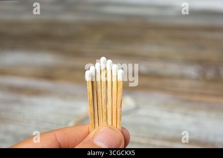 A closeup view of a hand holding a set of wooden match sticks against a wooden surface background. Stock Photo